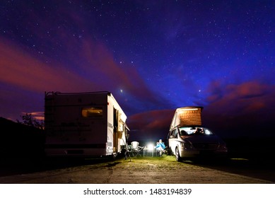 Campervans Are Parked On A Beach At Night Under Stars. A Man Camping With Two Camping Vans Is Enjoying The Evening Relaxation Under Thew Starry Night In Soesto Beach - Galicia, Spain.