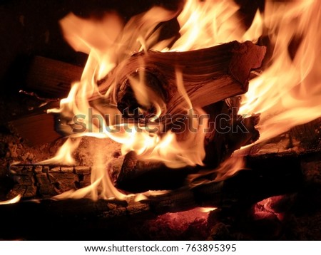 Campfire burning logs in large orange and yellow flames in close up of the wood aflame