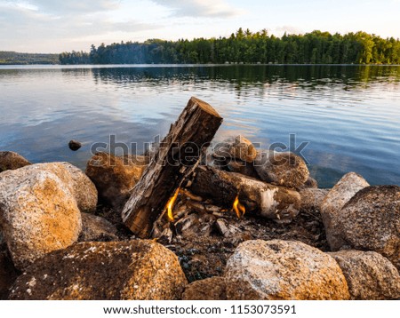 A campfire burning in a stone fire ring along the shore of a river in Maine.