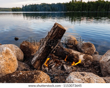 A campfire burning in a stone fire ring along the shore of a river in Maine.