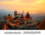 Campfire in the midst of nature. There is an Asian couple making coffee and playing music together while setting up a tent on a mountaintop with a view of nature in Thailand while the sun is setting.