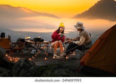 Campfire in the midst of nature. There is an Asian couple making coffee and playing music together while setting up a tent on a mountaintop with a view of nature in Thailand while the sun is setting. - Powered by Shutterstock