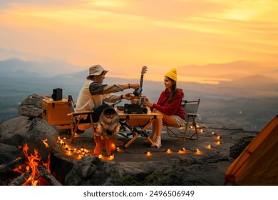 Campfire in the midst of nature. There is an Asian couple making coffee and playing music together while setting up a tent on a mountaintop with a view of nature in Thailand while the sun is setting. - Powered by Shutterstock