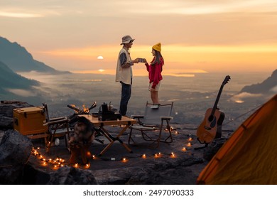 Campfire in the midst of nature. There is an Asian couple making coffee and playing music together while setting up a tent on a mountaintop with a view of nature in Chiang mai, Thailand - Powered by Shutterstock