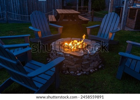 Campfire pit blazing fire surrounded by  adirondack chairs at night.