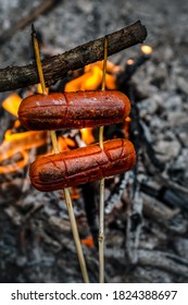 Campfire Sausage In Pan, Water Bottle And Titanium Mug Near The Fire Outdoors. Bushcraft, Adventure, Travel, Tourism And Camping Concept.