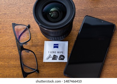 CAMPINAS, SÃO PAULO/BRAZIL - August 25, 2019: Zeiss Pre-moistened Lens Cleaning Wipe, Eyeglasses, Camera Lens And Smartphone On A Wooden Background