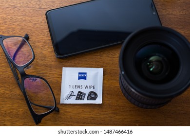 CAMPINAS, SÃO PAULO/BRAZIL - August 25, 2019: Zeiss Pre-moistened Lens Cleaning Wipe, Eyeglasses, Camera Lens And Smartphone On A Wooden Background