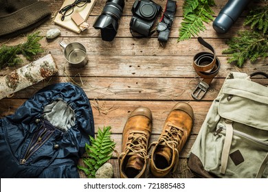 Camping Or Adventure Trip Scenery Concept. Backpack, Jacket, Boots, Belt, Thermos And Camera On Wooden Background Captured From Above (flat Lay). Layout With Free Text (copy) Space.