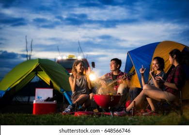 Camping Of Asian Man And Women Group, Relaxing, Sing A Song And Cooking, With Ligh From Car And Tent