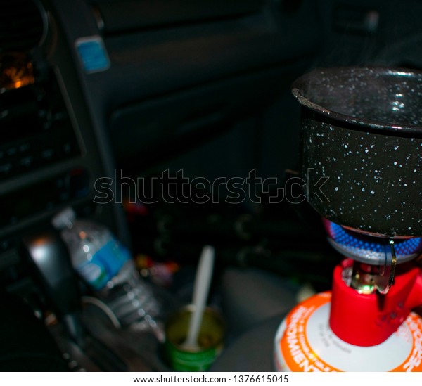 Camping Brewing Coffee in Car With\
Backpacking Single Burner Stove and Open Can of\
Beans