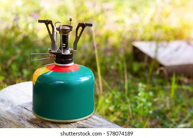 Camping burner installed on gas cylinder tank in background of summer forest. Compact kitchen stove for cooking hot food in field travel conditions. Adventure Park - Shutterstock ID 578074189