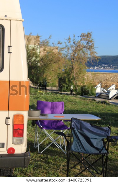 Camping car with camping chair and\
camping table, close to the sea, food on top af the table, summer\
with sun which is shining in Croatia, Europe,\
vanlife