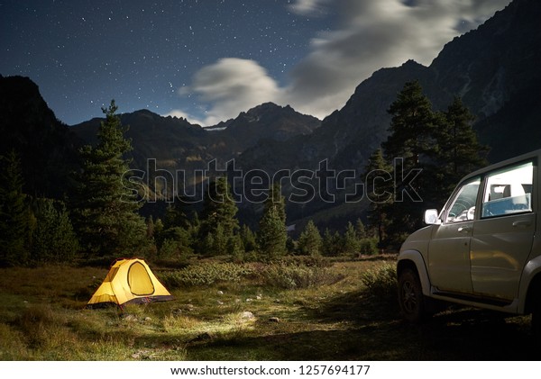 Camping with a car, yellow tent at night with\
moonlight at mountain\
area