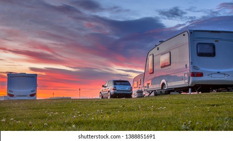 Camping caravans and cars parked on a grassy campground under beautiful sunset