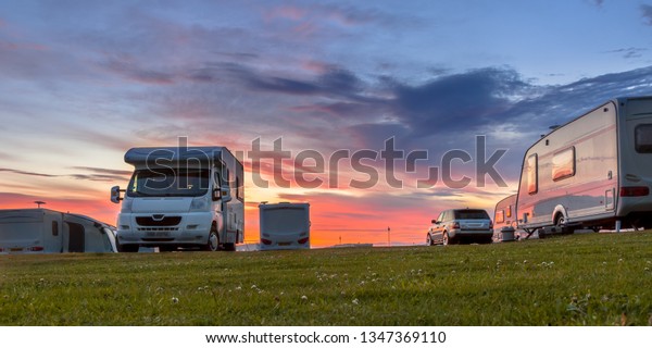 Camping caravans and cars parked on a grassy\
campground under beautiful\
sunset