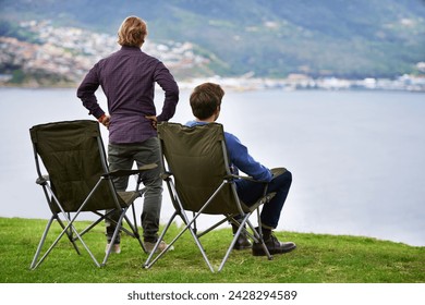 Camping, chair and people relax at lake with landscape in countryside, nature or calm vacation. Summer, holiday and back of friends sitting on grass at river with peace in environment together
