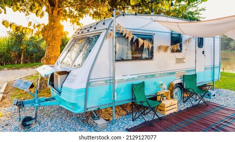 Camping chairs placed outside cozy retro travel trailer Caravan under tree before sunset near the river in peaceful countryside. Outdoor and Recreational Vehicles Theme. Travel Industry. - Shutterstock ID 2129127077