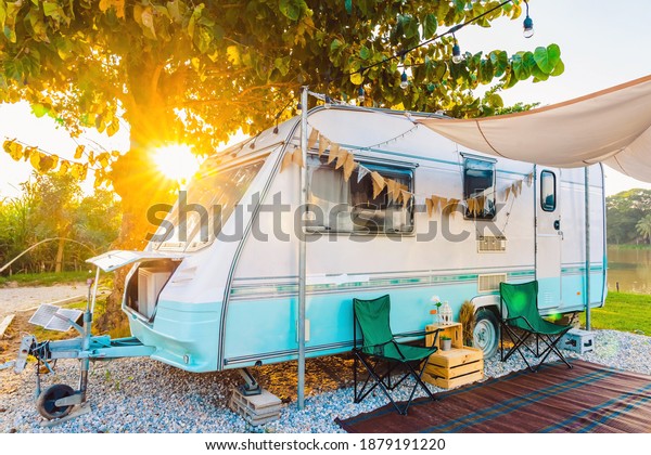 Camping\
chairs placed outside cozy retro travel trailer Caravan under tree\
before sunset near the river in peaceful countryside. Outdoor and\
Recreational Vehicles Theme. Travel\
Industry.