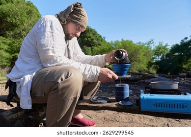 Camping coffee making process: an hispanic traveler pours hot water into a folding travel filter with freshly ground coffee to prepare his breakfast at his campsite, outdoors.