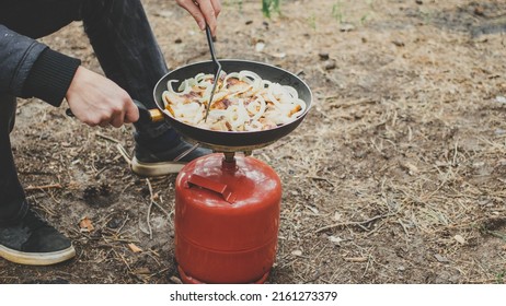 Camping cooking with steam in forest. Man fry bacon in pan on portable gas stove outdoor. Preparing dinner picnic during hike. Touristic campsite lifestyle concept.