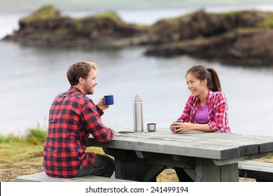 Camping couple sitting at table drinking coffee from thermos bottle flask by lake on Iceland. Campers woman and man relaxing taking break on road trip in beautiful Icelandic nature. - Powered by Shutterstock