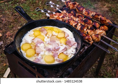 Camping cuisine: chicken egg with a bright yolk on a cast-iron pan in a campfire close-up, camping breakfast bacon egg, tourist breakfast on open fire