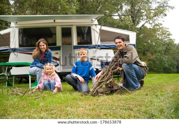 Camping: Cute Family Poses By Campfire Near\
Pop-Up Trailer