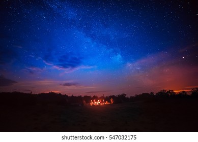 Camping fire under the amazing blue starry sky with a lot of shining stars and clouds. Travel recreational outdoor activity concept. - Powered by Shutterstock