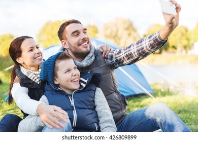 Camping, Hike, Technology And People Concept - Happy Family With Smartphone Taking Selfie At Campsite