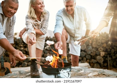 Camping, Hiking And Adventure Senior People Melting Marshmallows In A Camp Fire During A Nature Retreat Or Getaway Outdoors. Happy Retired Or Senior Group Of Friends Enjoying Fun Recreation Activity