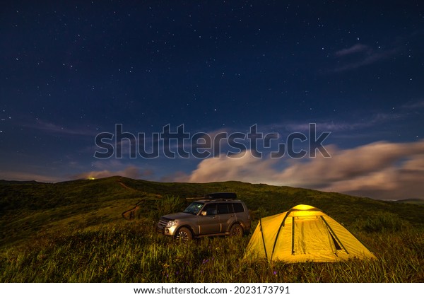 Camping in a meadow under night sky. Some noise\
from high ISO exists.