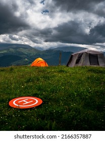 Camping In The Mountains With Tent Standing On A Hill, Night And Sunset Landscape With Helipad For Drone