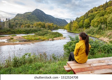 Camping nature woman sitting at picnic table enjoying view of wilderness river in Quebec and autumn foliage forest, Canada travel. Parc de la Jacques-Cartier, Quebec.