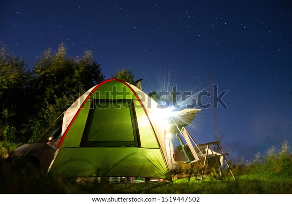 Camping at night, tent with chairs and a car\
in background. Campering under starry\
sky.