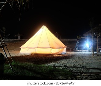 Camping on the beach at night bright orange lights in a white tent Under the stars at night on a weekend vacation.