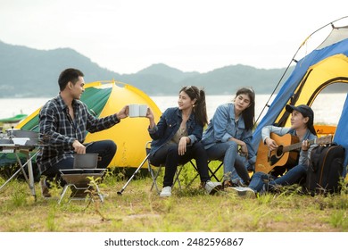 Camping outdoor. Group  friends camping leisure and destination travel. Family sitting around camp fire and playing guitar and roasted sausages, tourism relax and travel near river in holiday. - Powered by Shutterstock