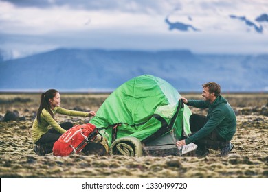 Camping people outdoor lifestyle couple tourists putting up a tent in nature lansdcape at dusk. Campers with backpacks setting up their campsite for the night in mountain summer background. - Powered by Shutterstock