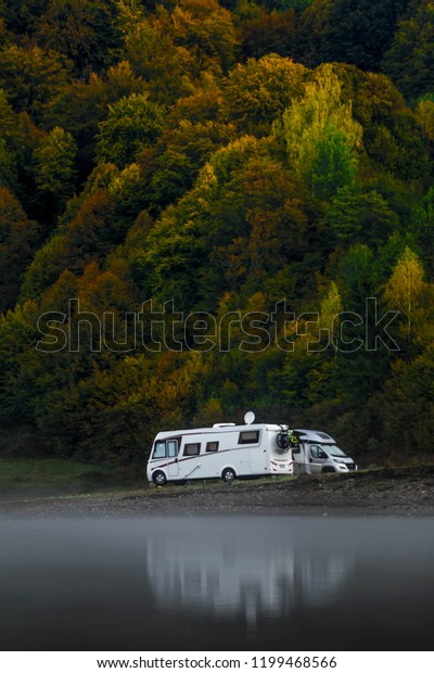 Camping site on a lake with\
caravans in the background nice autumn trees. Family vacation\
travel, holiday trip in motorhome, Caravan car Vacation. Misty\
morning.