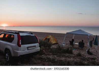 Camping Site At Sandy Beach. People Sitting And Looking On Sunset. Summer Travel Destination