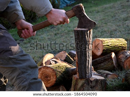 camping skills father with son. chopping wood logs from willow in autumn. the father shows with ax what can happen like cutting off an arm, fingers, foot. in the background wooden beehives beekeeper