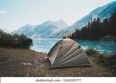 Camping Tent In Campground At National Park. Tourists Camped In The Woods On The Shore Of The Lake On The Hillside. View Of Tent On Meadow In Forest. Camping Background