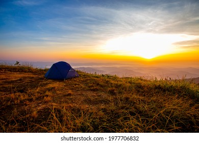 Camping Tent In Campground At National Park. Tourists Camped In The Woods On The Shore Of The Lake On The Hillside. View Of Tent On Meadow In Forest. Camping Background