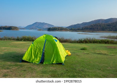 Camping Tent In Campground At National Park. Tourists Camped In The Woods On The Shore Of The Lake On The Hillside. View Of Tent On Meadow In Forest