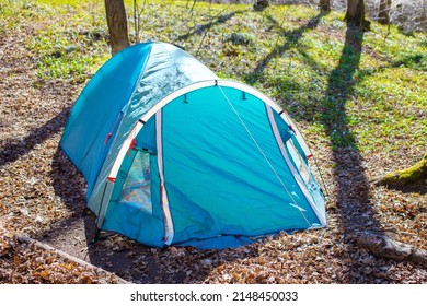 Camping Tent In Campground At National Park. Tourists Camped In The Woods On The Shore Of The Lake On The Hillside. View Of Tent On Meadow In Forest. Camping Background.