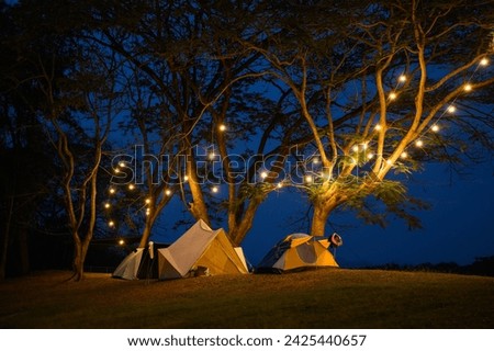 camping tent on grass courtyard and warm night light under dark blue sky. Family vacation picnic on holiday relax
