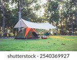 Camping tent is set up in a grassy field with a canopy over it. A couple of chairs are set up in front of the tent.
