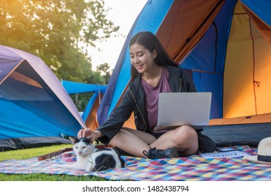 Camping And Tent Vacation Concept.Asian Women, Adventure Travelers, Hiking Sitting And Play Laptop Computer Have With Cat At Tent Camping In Forest.