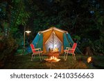 Camping tents at night, vintage cabin tents, antique oil lamps, retro chairs, and a group of camping tents with outdoor coffee-making facilities on wooden tables in a forest camping area in the forest