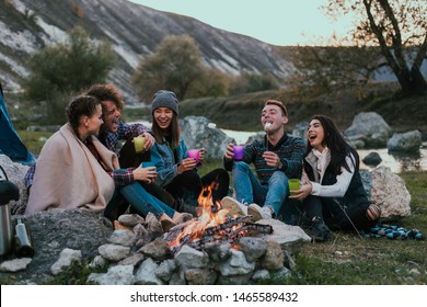 Camping time for a big group of friends sitting beside the fireplace and enjoying the time together in the middle of nature - Powered by Shutterstock